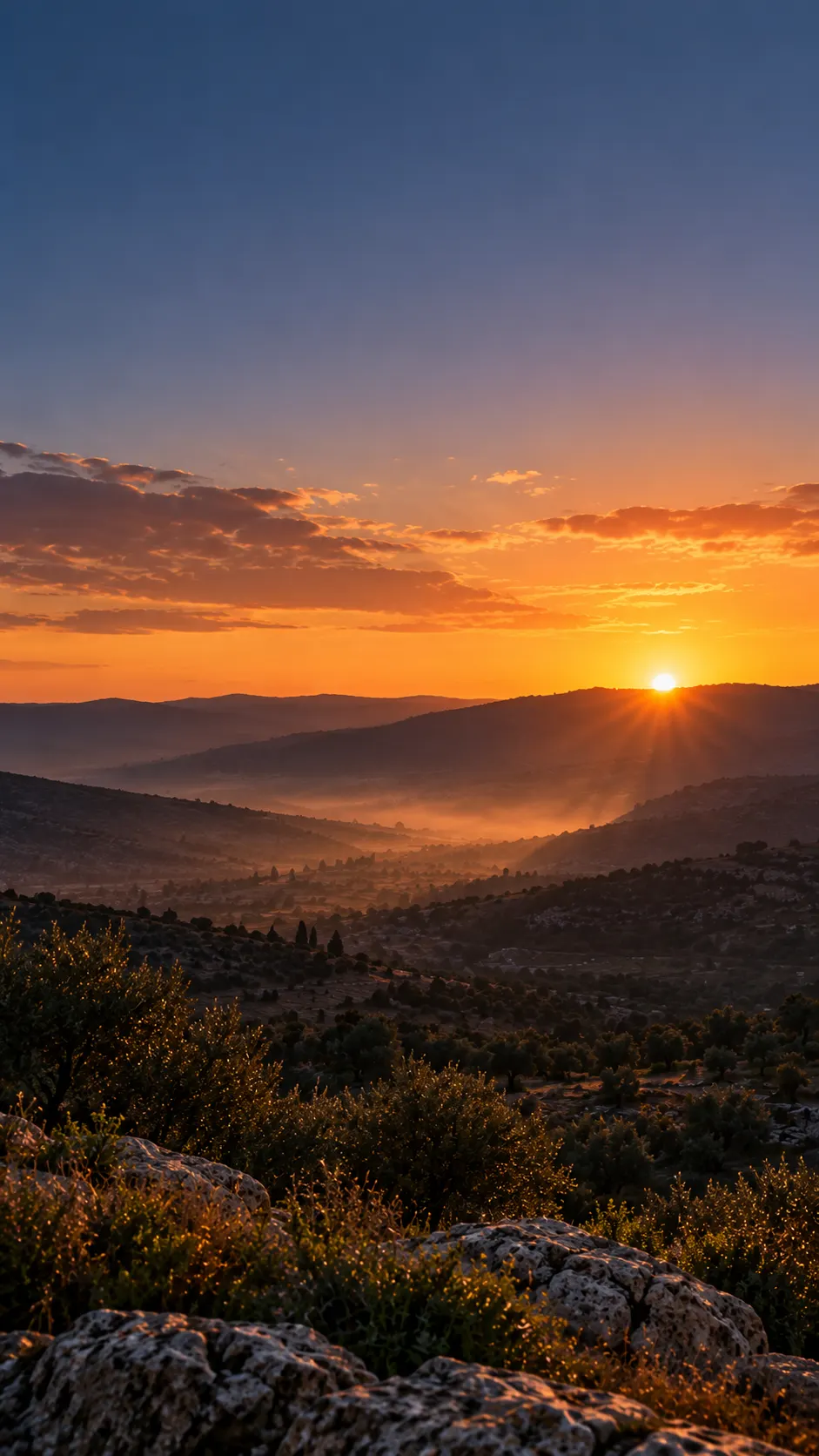 Sunrise breaking over a dark horizon, light spreading across a valley.